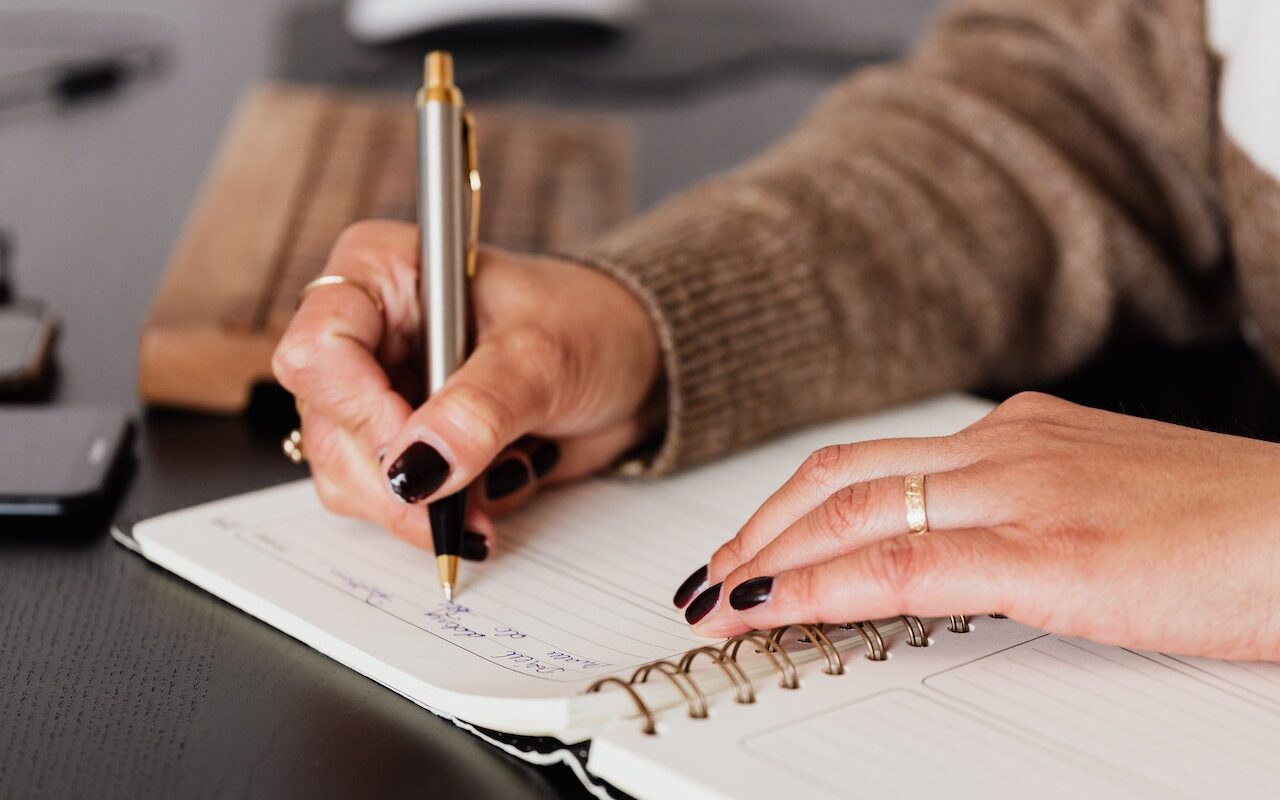 Mani che scrivono su un quaderno per appuntare le informazioni più importanti da memorizzare su un argomento.