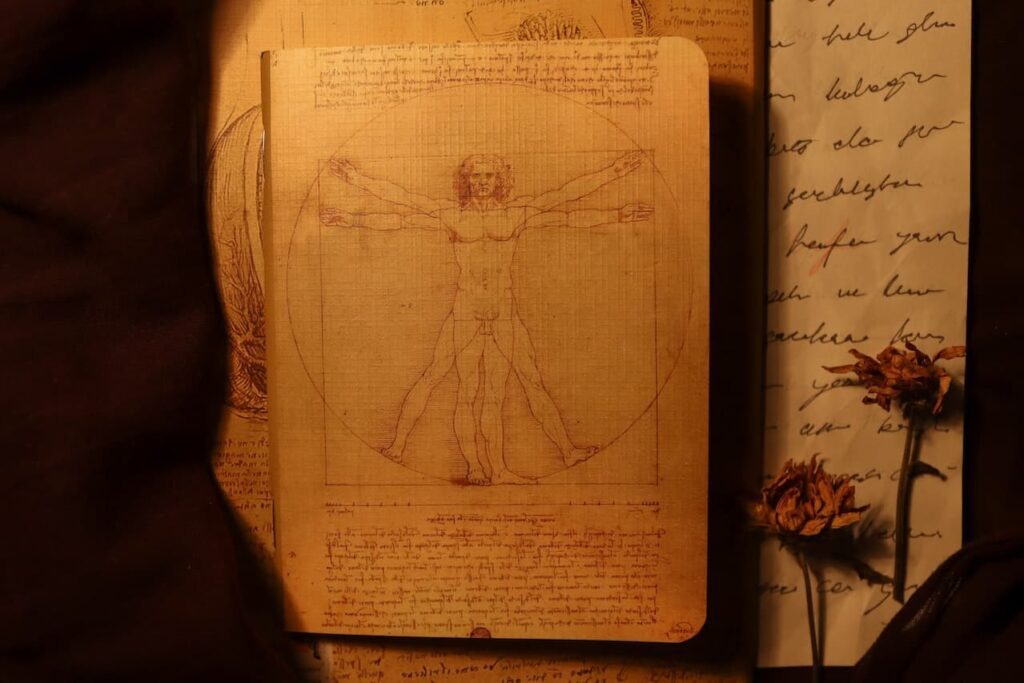 Manoscritto con la rappresentazione di "L'uomo vitruviano". L'opera è un disegno a penna e inchiostro su carta di Leonardo da Vinci, conservato, ma non esposto, nel Gabinetto dei Disegni e delle Stampe delle Gallerie dell'Accademia di Venezia. Nella foto ci sono dei fiori secchi su un mano scritto (a destra) e un'ombra ( a sinistra).