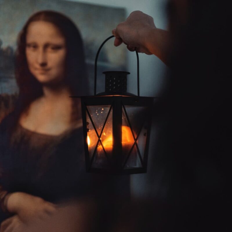 Arte e medicina sono collegati fin dai tempi della gioconda, ma anche prima. Nell'immagine c'è Monna Lisa sullo sfondo. A destra una striscia nera come un'ombra da cui esce una mano che tiene una lanterna.