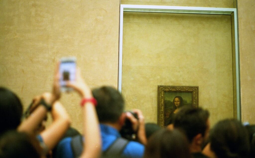 Monna Lisa nel museo del Louvre con una folla di persone intenta a fotografare il quadro. Nessuno solitamente pensa alla combinazione tra arte e medicina dietro questo quadro. Nell'immagine c'è un muro giallo con il quadro della gioconda sullo sfondo.