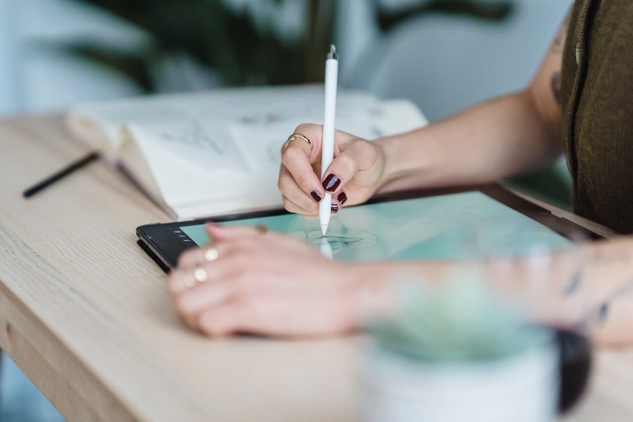Mano che scrive su un tablet. Vicino al dispositivo c'è un libro aperto.