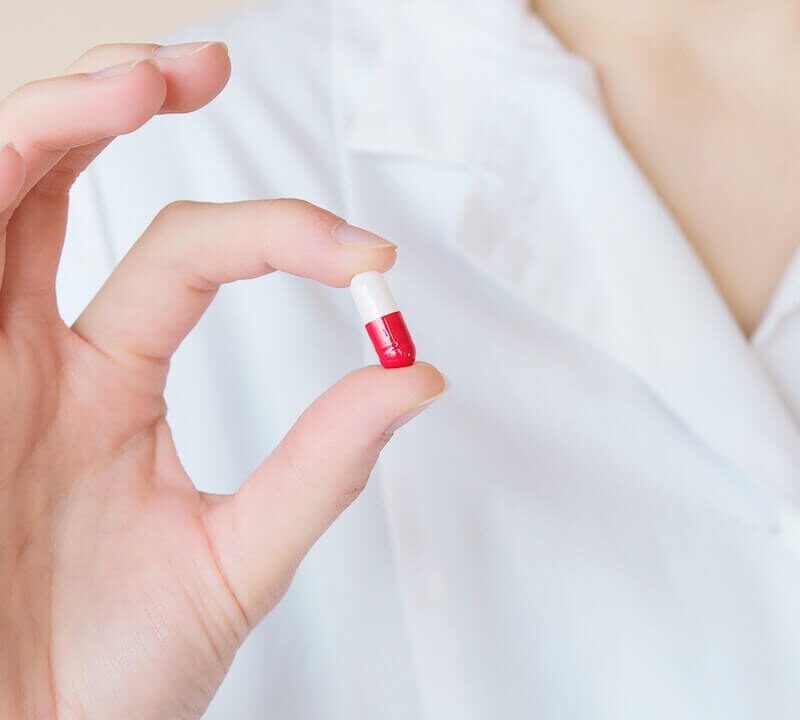 Farmacista con pillola rossa e bianca tenuta tra pollice e indice.