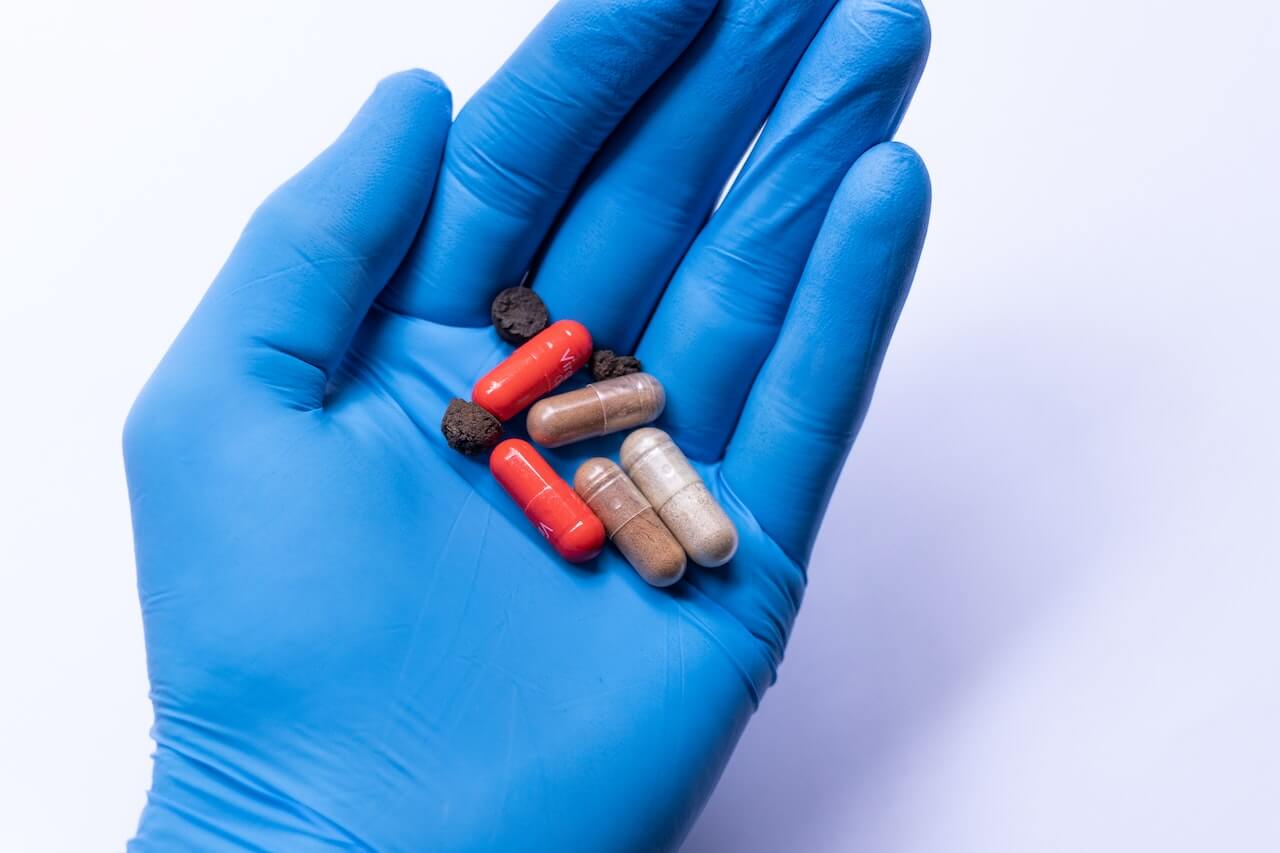 Guanto blu in lattice indossato da un farmacista che tiene in mano opercoli e pillole.