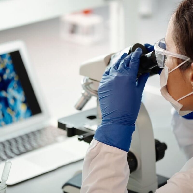 Laureata in biotecnologie mentre analizza un campione utilizzando il microscopio e il computer.