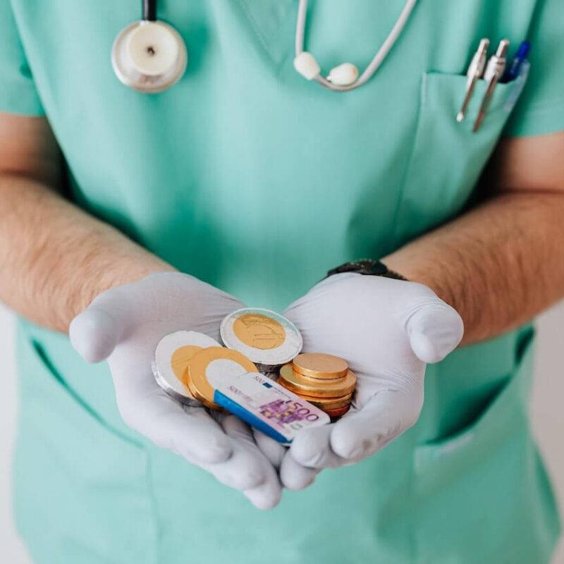 Logopedista con in mano il suo stipendio fatto di soldi di cioccolata per far capire le variazioni che possono esserci. Indossa uno scrub verde, guanti bianchi e si intravede uno stetoscopio appeso al collo.