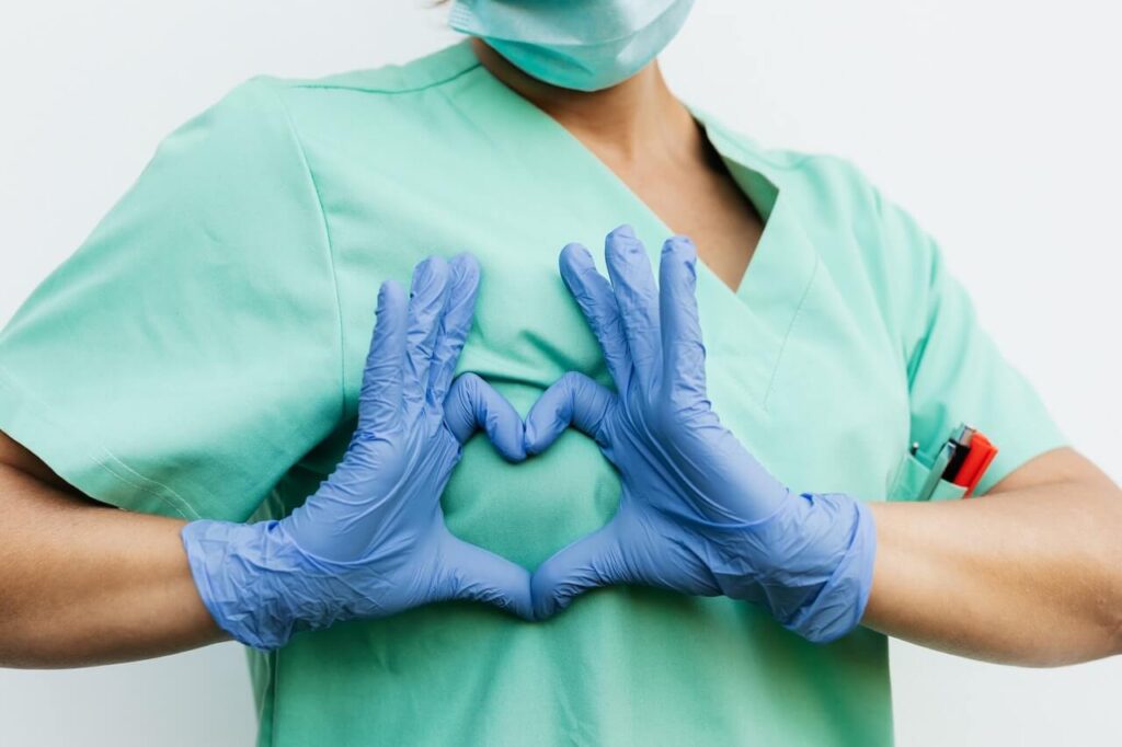 Scrub verde da medico o infermiere con le mani a forma di cuore mentre indossano i guanti blu per gli ambienti sterili.