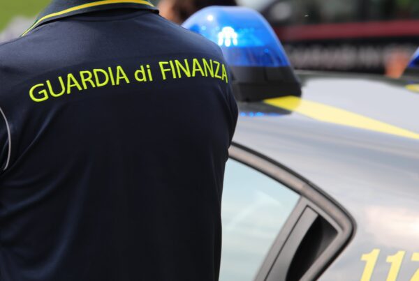 Agente della guardia di finanza appostato vicino a una volante delle fiamme gialle.