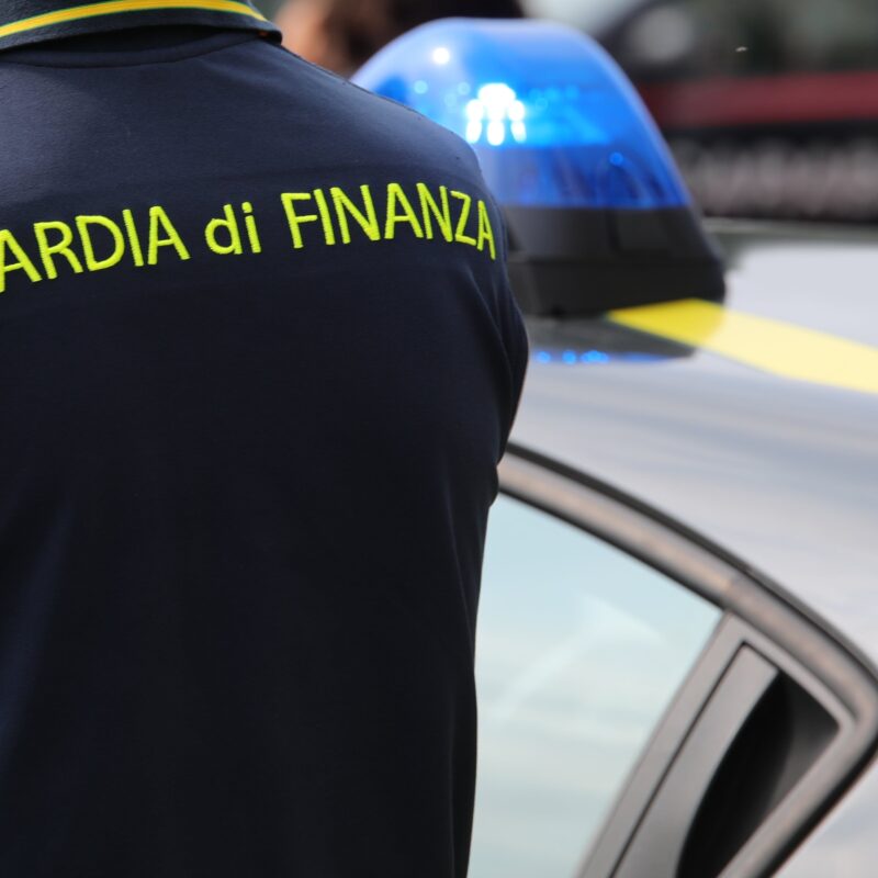 Agente della guardia di finanza appostato vicino a una volante delle fiamme gialle.