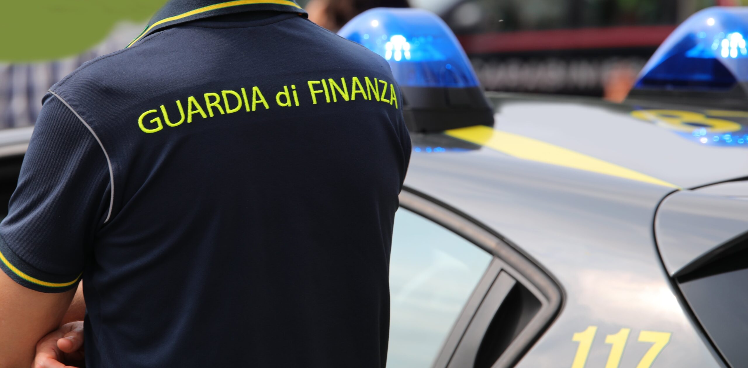 Agente della guardia di finanza appostato vicino a una volante delle fiamme gialle.