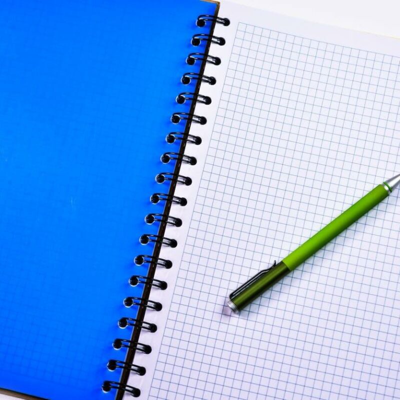 Quaderno con fogli a quadretti e una penna poggiata sulla pagina.