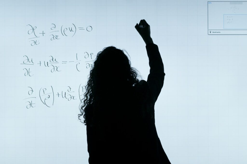 Ragazza che scrive su una lavagna bianca per annotare delle formule matematiche.