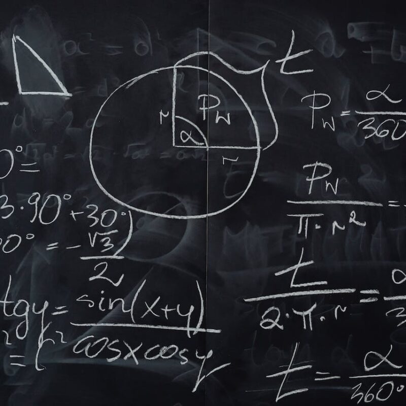 Lavagna nera con scritte in gesso bianco per calcolare gli angoli sulla circonferenza goniometrica.