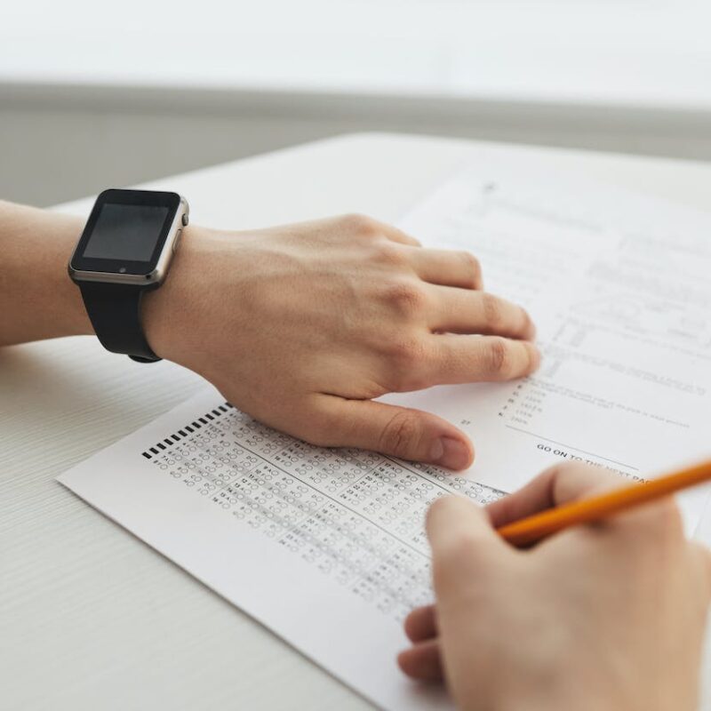 Test cartaceo a crocette. Una mano mantiene il foglio risposte mentre l'altra segna i risultati su un altro foglio con una matita.