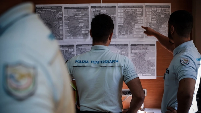 Due agenti che indicano su un foglio attaccato al muro i gradi di polizia penitenziaria