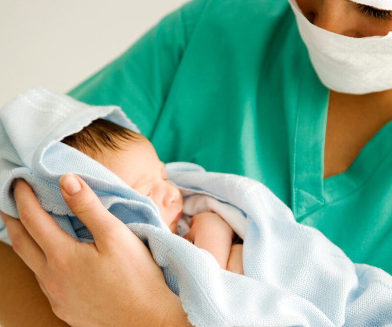 Un'ostetrica in camice che tiene un neonato avvolto in una coperta in un reparto di maternità.