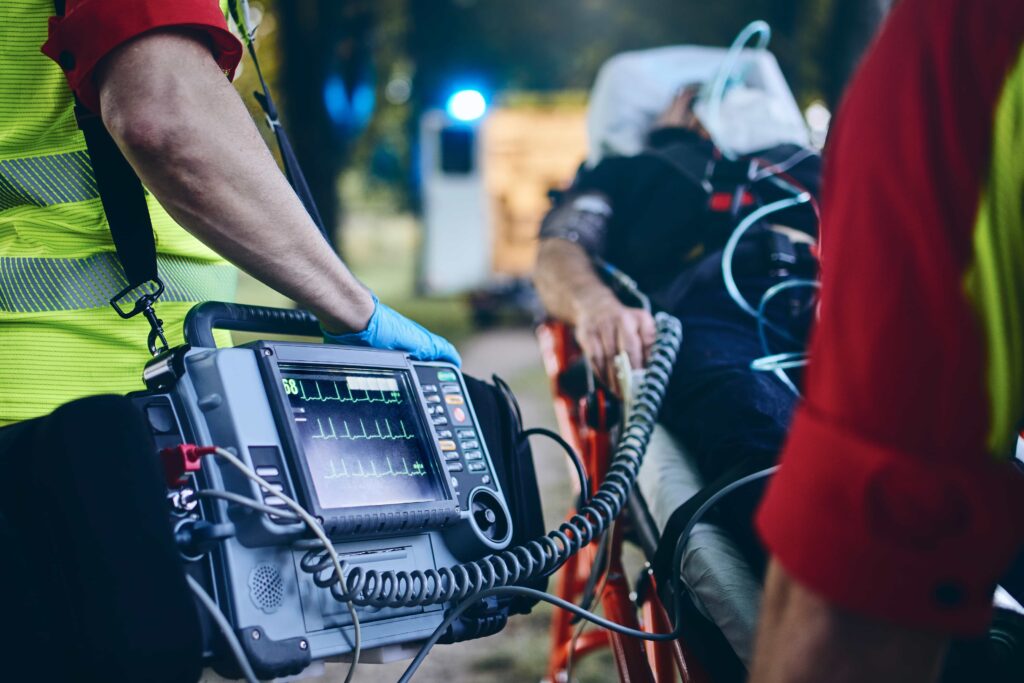 Medici d'emergenza mentre trasportano un paziente in barella e osservano i parametri vitali su un monitor.