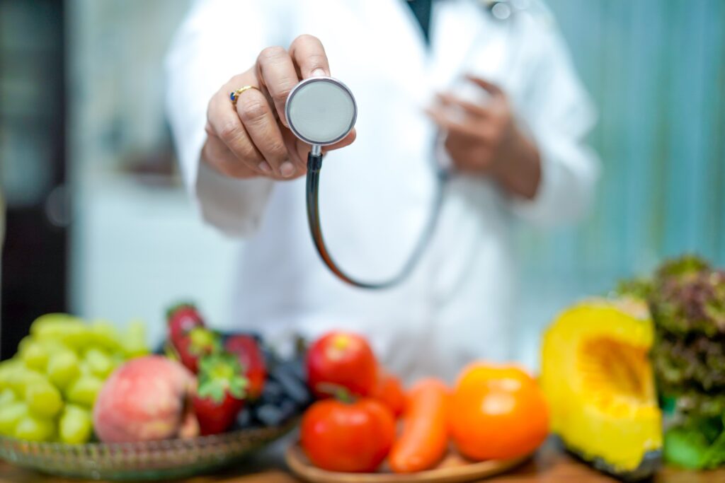 Medico in Scienza dell'Alimentazione che tiene in mano lo stetoscopio e ha di fronte a se gli alimenti per un'alimentazione sana.