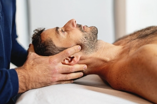osteopata visita un paziente in studio eseguendo una manovra cranica