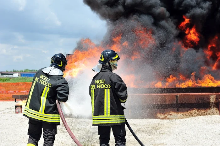 Due Vigili del Fuoco impegnati nello spegnimento di un incendio durante un'esercitazione, un'immagine rappresentativa di cosa significa intraprendere il percorso su Come diventare Vigile del Fuoco.