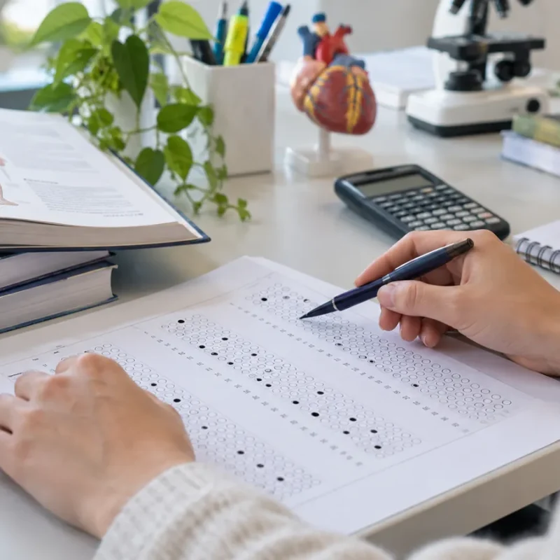 Studentessa compila il foglio risposte del test di Professioni Sanitarie 2026 accanto a un manuale di anatomia