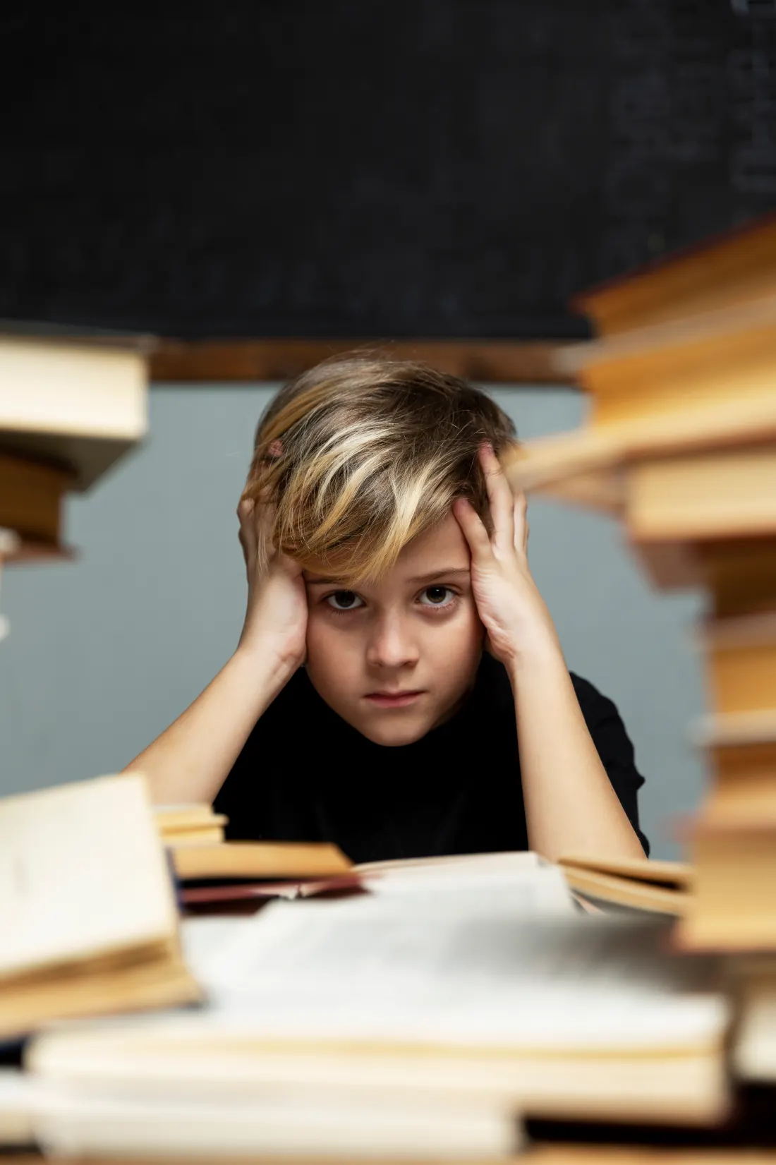Un bambino stressato sommerso dai libri di studio